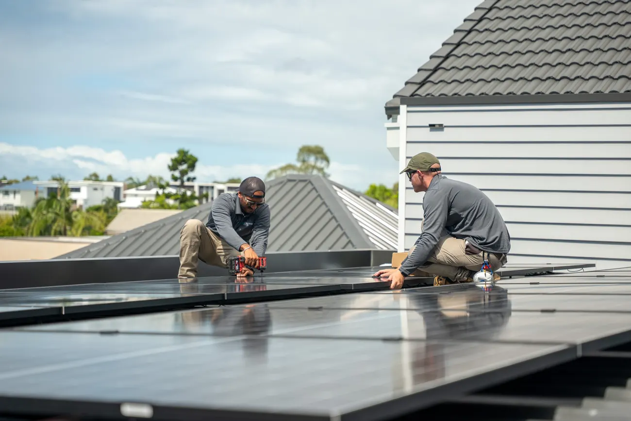 Two LuxGrid installers fitting solar panels on a Hope Island roof